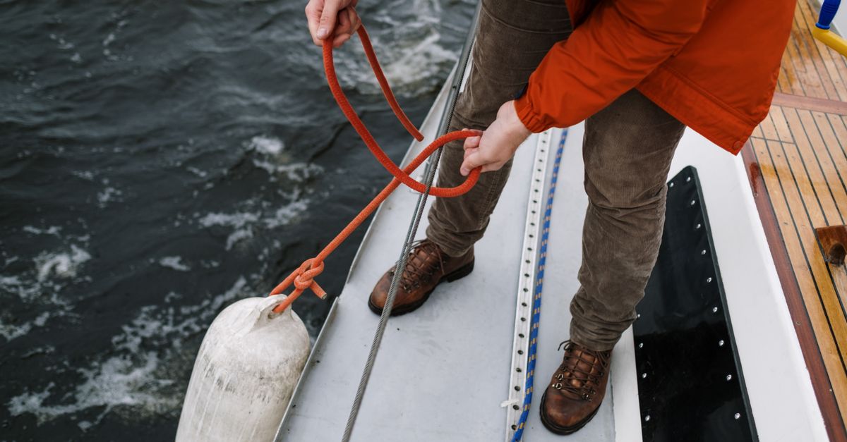 A person tying a rope to secure a buoy on a boat, showcasing boating skills and safety.